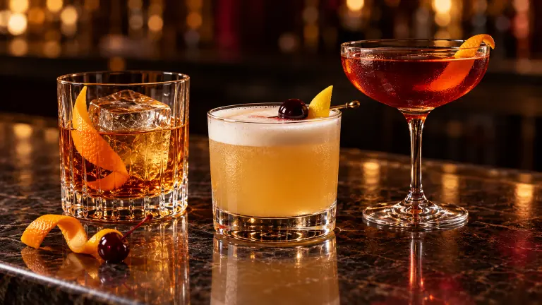 Old Fashioned, Whiskey Sour and Boulevardier on a dark bar counter